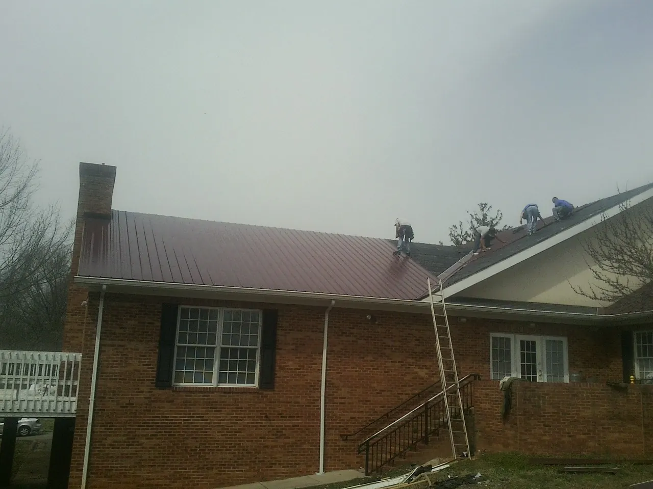 Crew setting red metal roofing panels on a brick home in Mount Pleasant